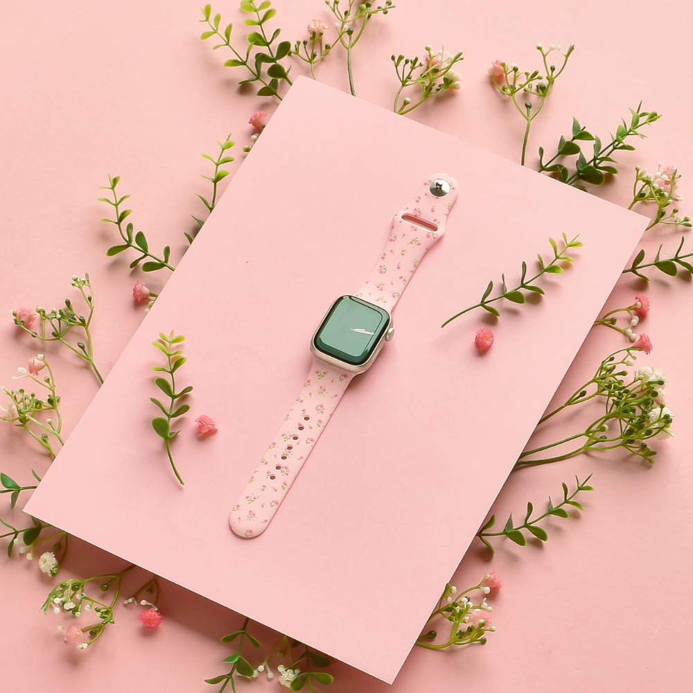 Pink Apple Watch strap with a ditsy floral pattern of green leaves and white flowers.