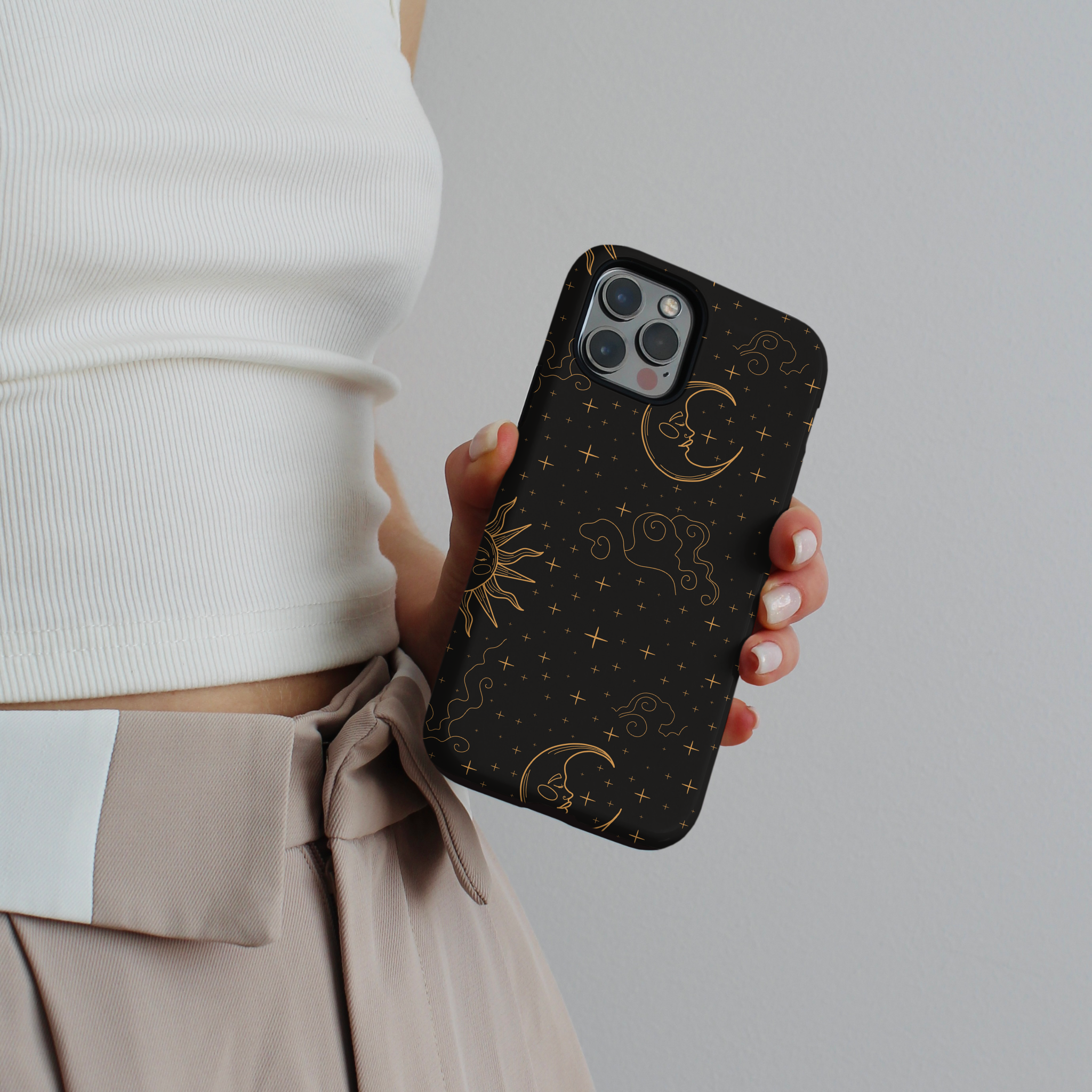 Tough phone case with gold stars, moons, and suns on a black background, held by a person in a white top.
