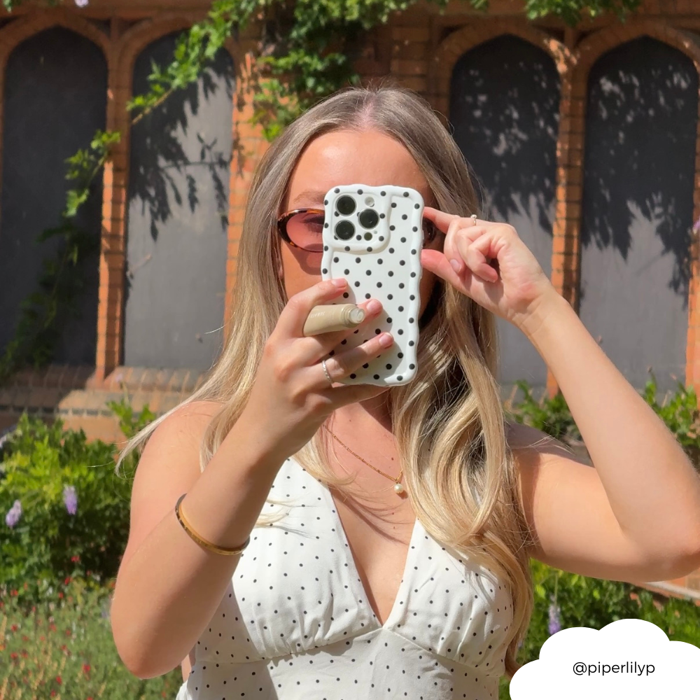 Woman outdoors holding Coconut Lane wavy phone case with white polka dot pattern, partially covering her face.