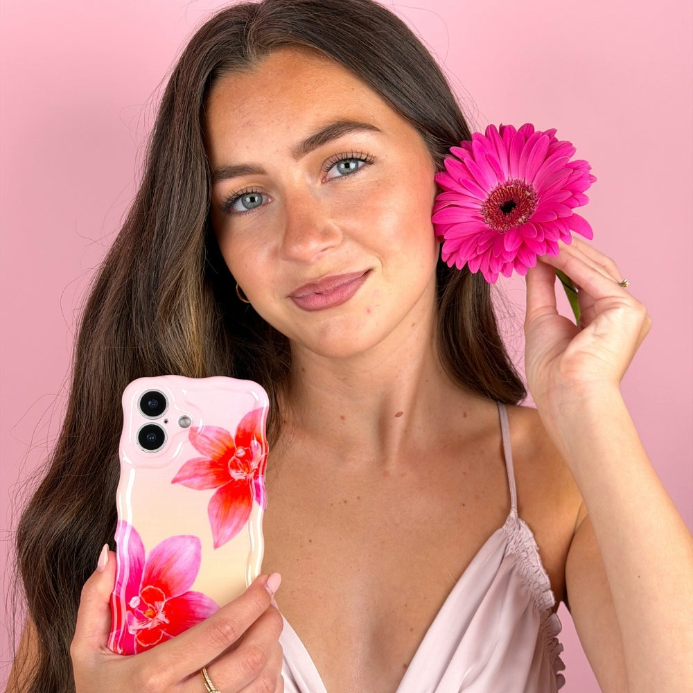 Woman holding a phone with a floral case and a pink flower against a pink background