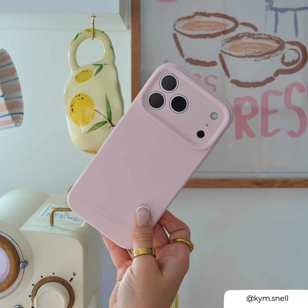 a women holding an iphone in a pastel pink phone case with coffee mug and photo frame as a backdrop