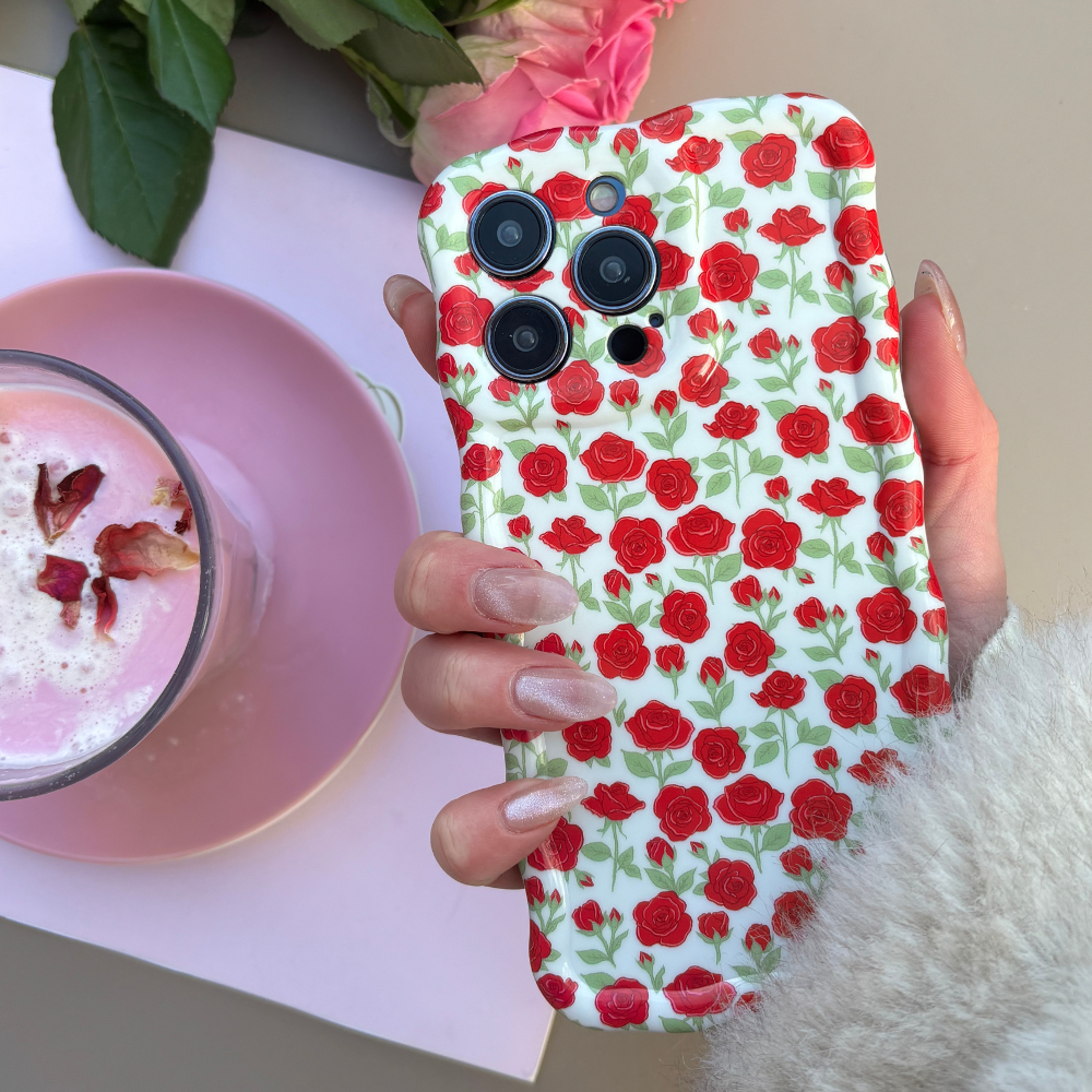 Hand holding a crimson wavy phone case with rose design next to a pink latte in a clear glass cup and saucer.