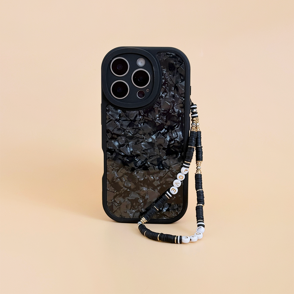 Black iPhone with a black and gold beaded phone strap on a beige background.