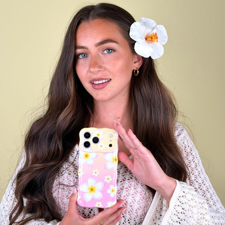 Girl with flower in long hair, holding Aloha Bloom Phone Case on yellow background.