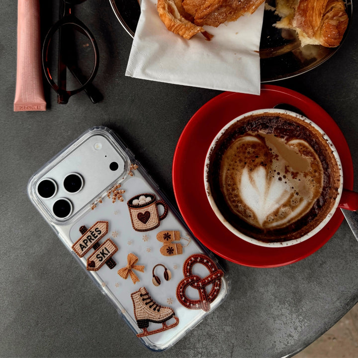 Phone with Apres hour phone case laid on table next to coffee, pastry and lipgloss