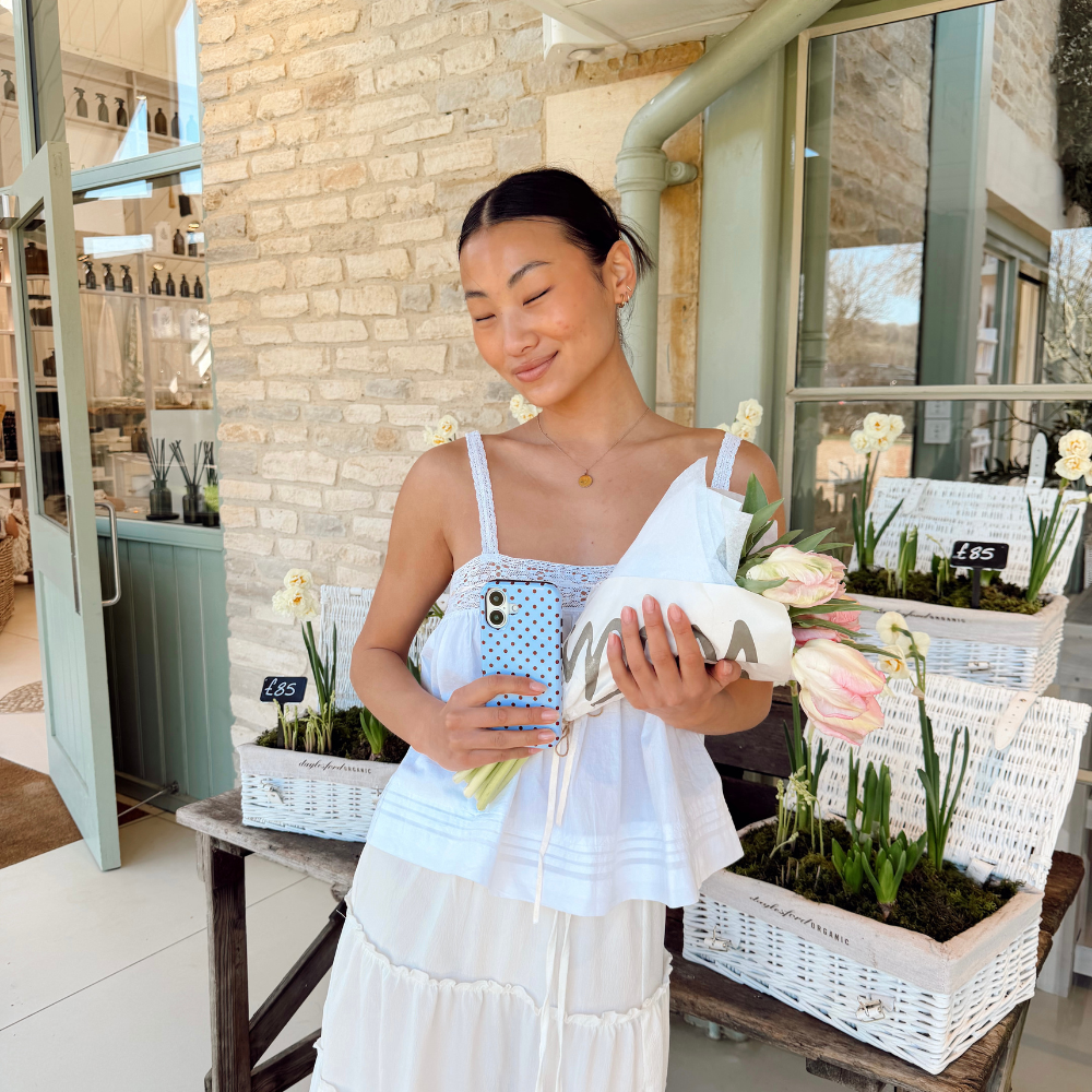 Girl in spring skirt holding her brown and blue polka dot phone case with flowers next to baskets