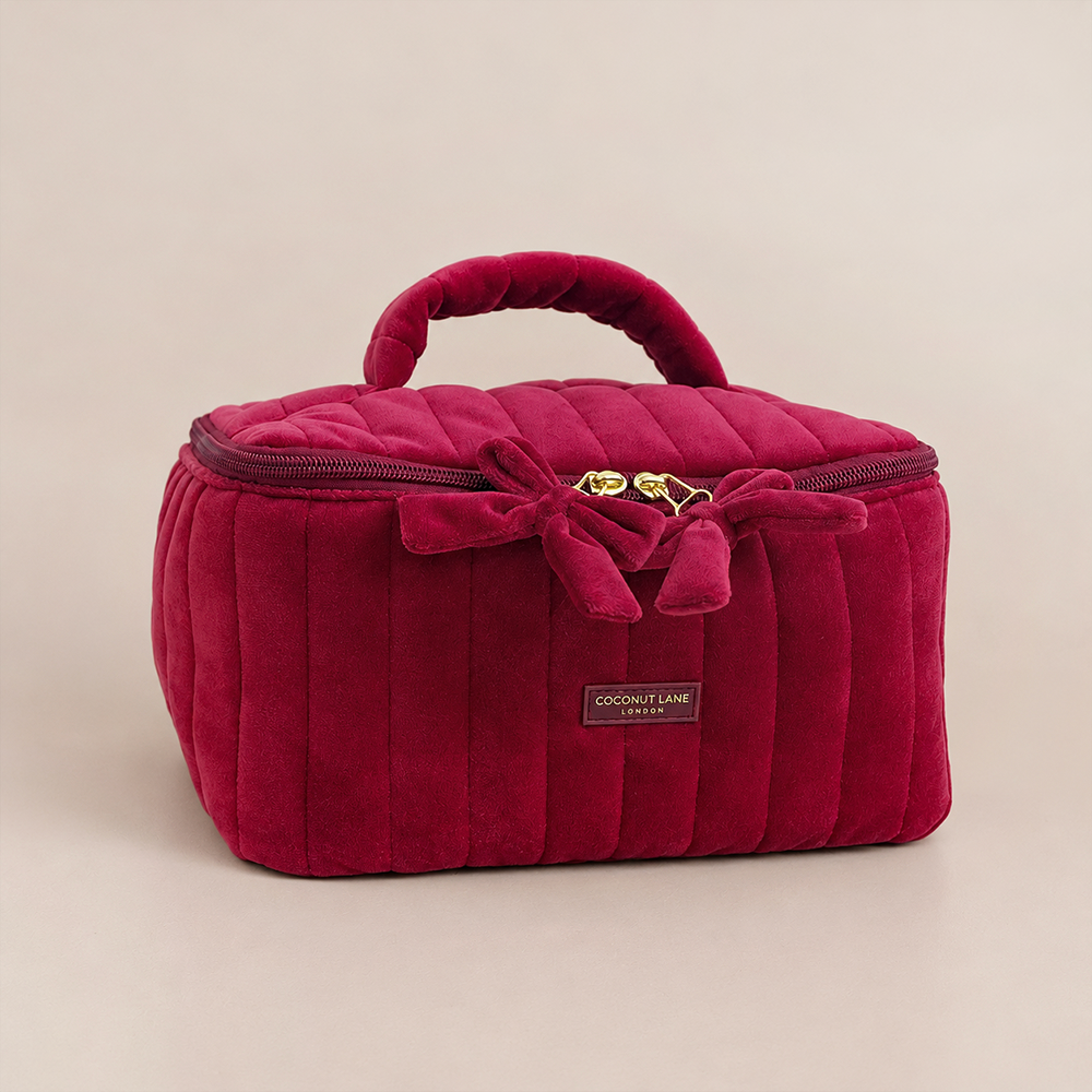 Burgundy velvet cosmetic bag with a quilted design, top handle, bow detail, and gold-tone hardware.