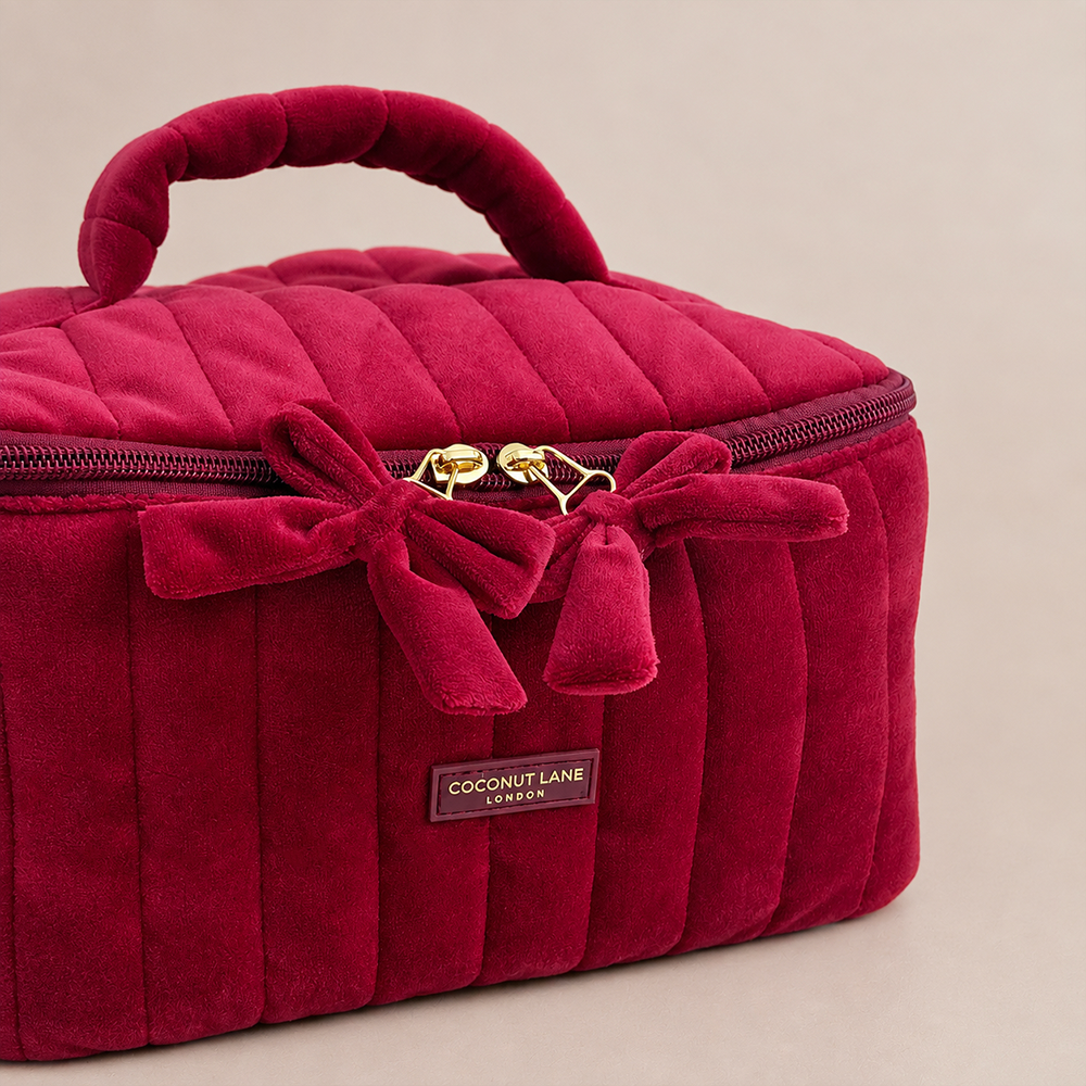 Burgundy velvet cosmetic bag with a quilted design, top handle, bow detail, and gold-tone hardware.