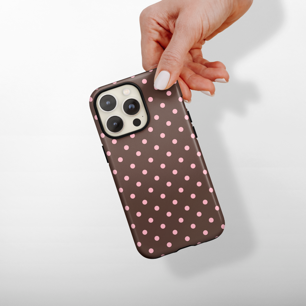 Hand holding a Coconut Lane Tough MagSafe phone case in brown with pink polka dots.