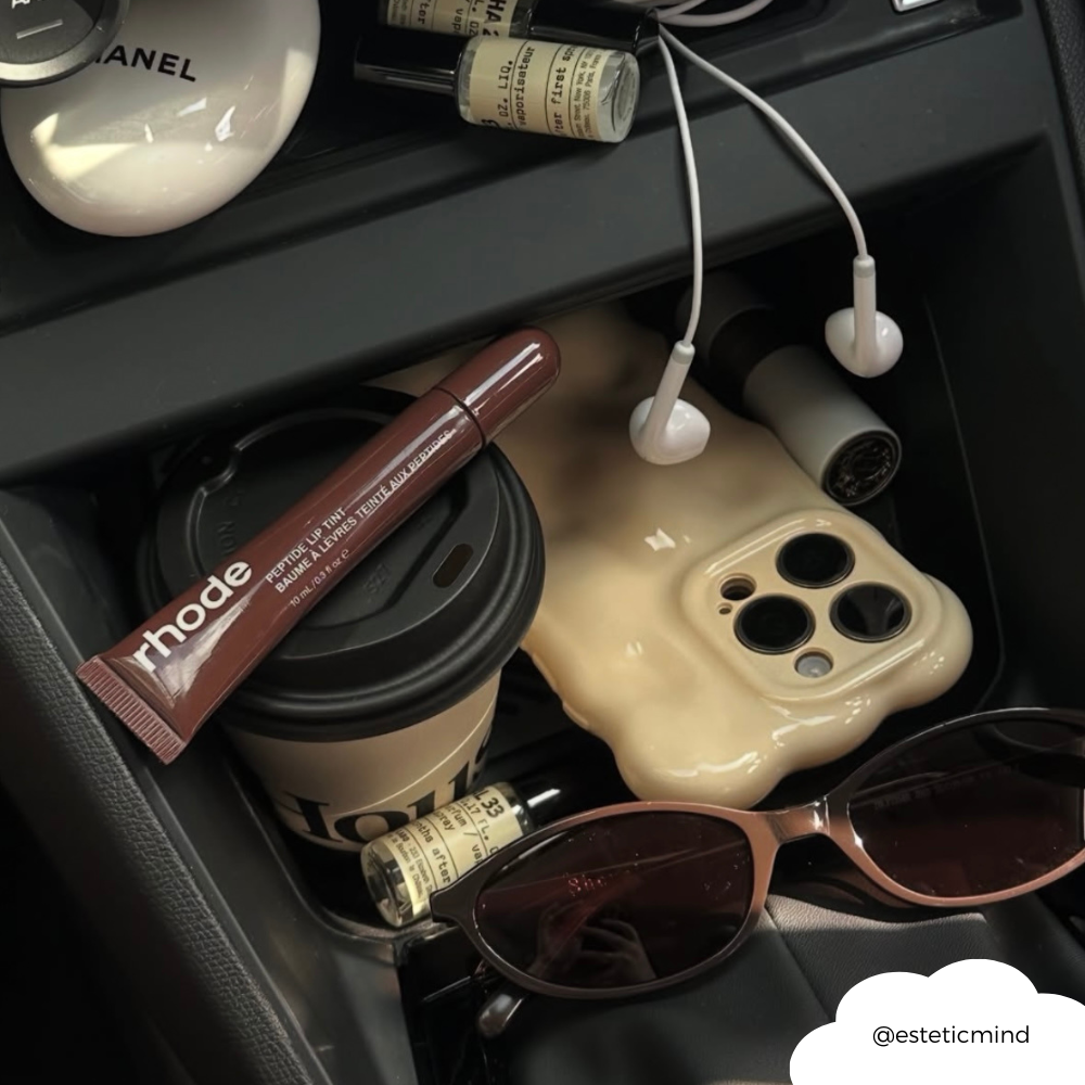 Butter yellow 3D bubble phone case, Chanel compact, coffee cup, sunglasses, lip tint, and perfume on car console.