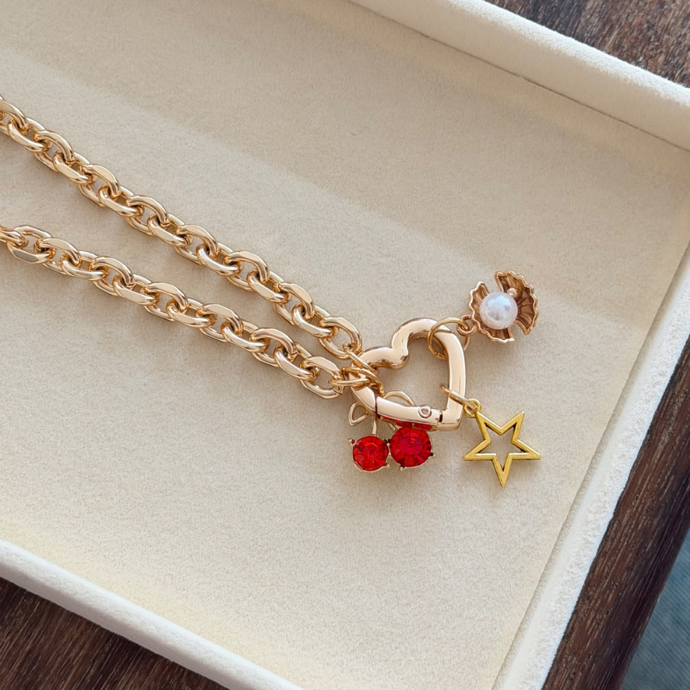 Gold Phone Charm with heart, cherry, and star charms on a beige background