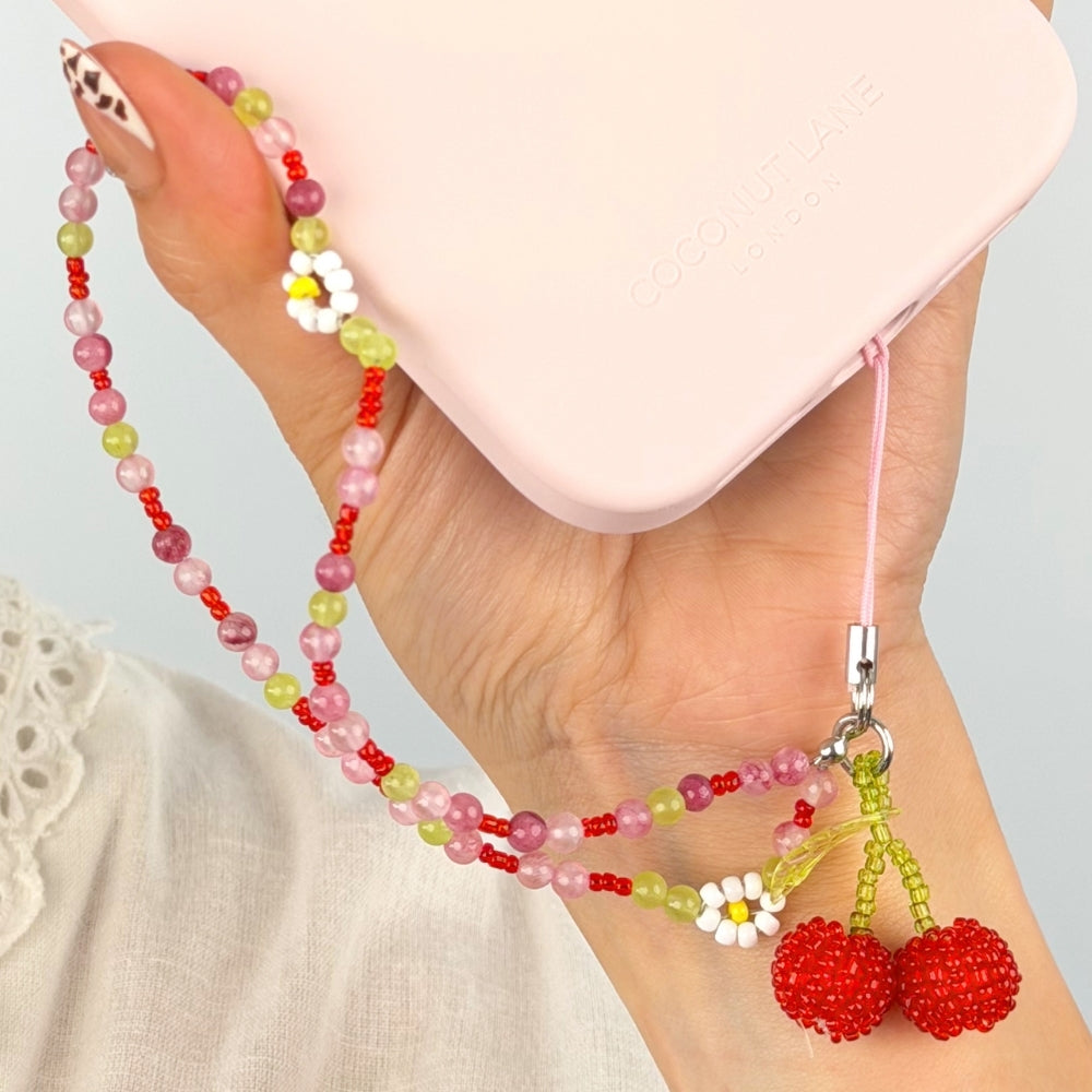 Colorful beaded cherry bomb phone strap with cherry charm and flowers, held by a hand against a light background