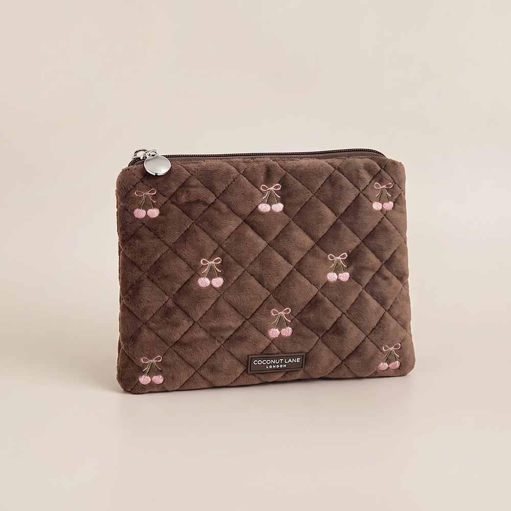 Brown quilted velvet zip pouch with pink embroidered cherries tied with bows, and a “Coconut Lane London” label at the bottom.