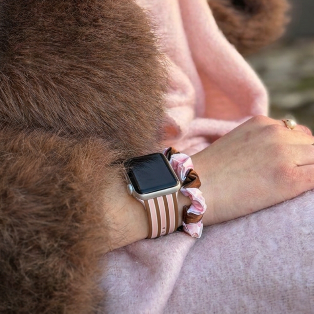 Pink and Brown stripes silicone sport band, attached to a black Apple Watch smartwatch on a woman's wrist alongside a matching cocoa and pink striped satin scrunchie.