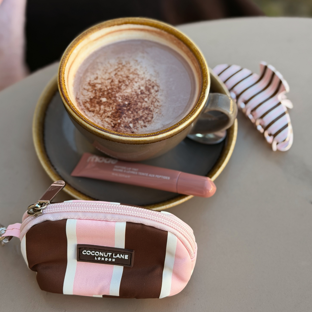 Coconut Lane Cocoa & Pink Stripe mini keyring bag featuring chocolate brown, baby pink and white stripes, placed on a table alongside a coffee and the matching cocoa and pink stripes claw clip.