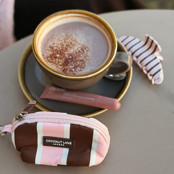 Coconut Lane Cocoa & Pink Stripe mini keyring bag featuring chocolate brown, baby pink and white stripes, placed on a table alongside a coffee and the matching cocoa and pink stripes claw clip.