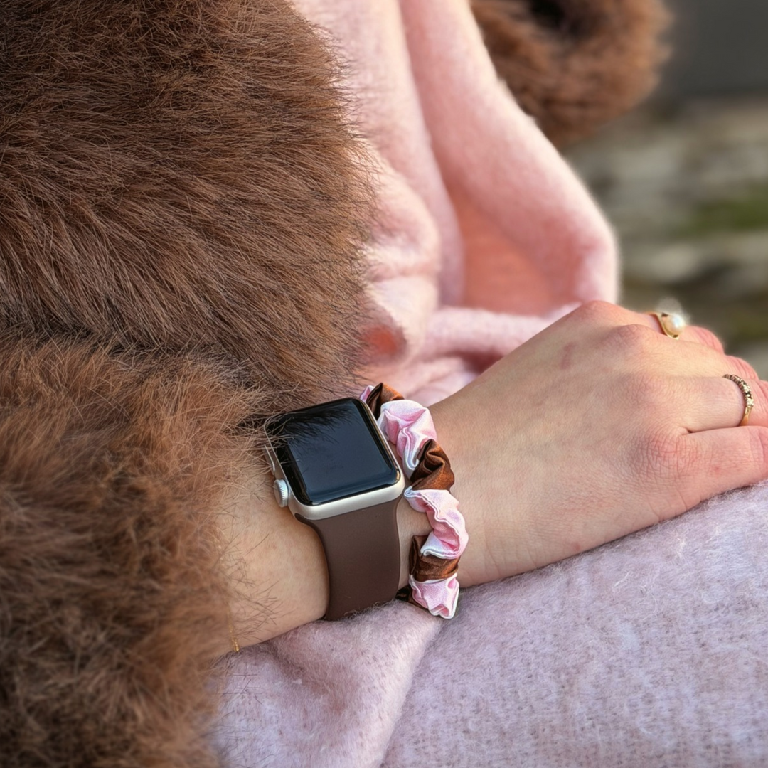 Nakd chocolate brown stipes silicone sport band, attached to a black Apple Watch smartwatch on a woman's wrist alongside a matching cocoa and pink striped satin scrunchie.