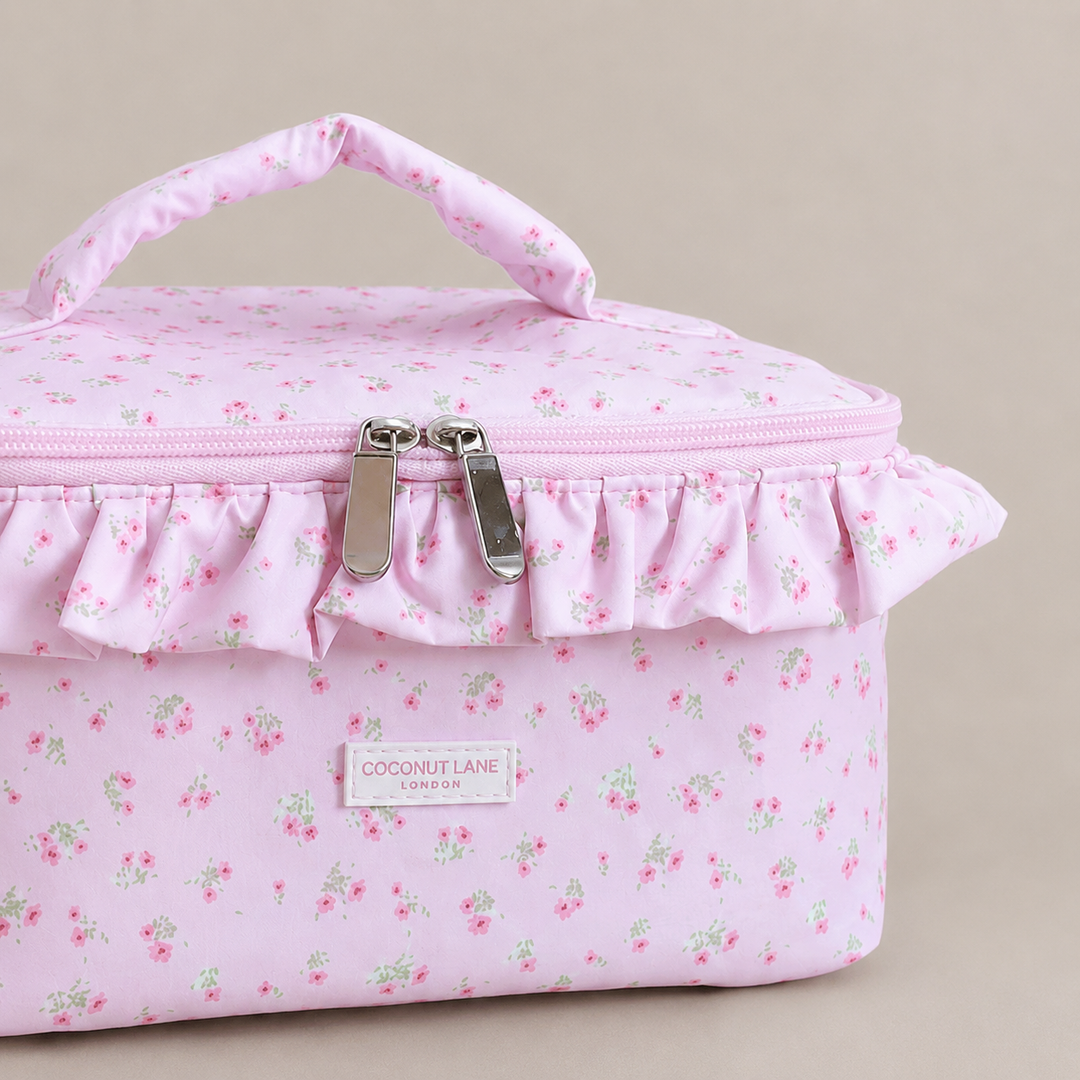 Pink floral patterned Vanity Bag with ruffled trim, handle and zip closure.