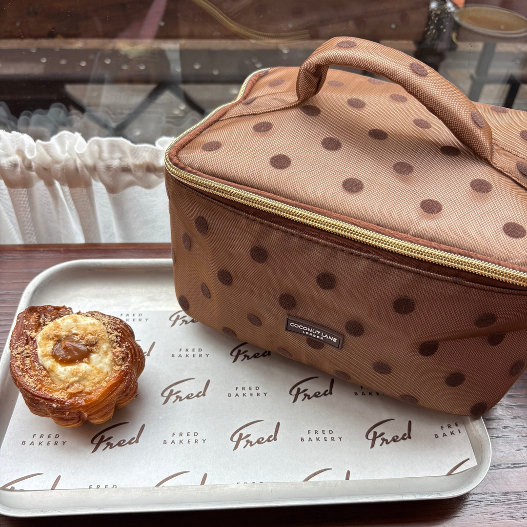 Flat lay cafe photo of the Dot Society chocolate brown vanity case. The vanity case is a brown mesh material with brown polka dot detailing. 