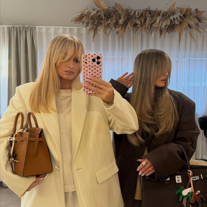Woman with blonde hair taking a mirror selfie. She is holding an iphone in a wavy baby pink phone case with brown polka dots. 