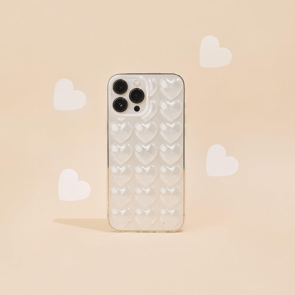 An iPhone 15 with a Coconut Lane 3D Hearts Phone Case - Clear stands upright against a peach-colored background. Light white heart shapes surround the phone, creating a whimsical and romantic atmosphere.