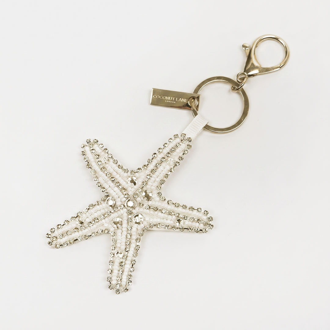 A starfish-shaped keyring made up of white and silver beads and rhinestones on a white background, attached to a gold-tone key ring and clasp.