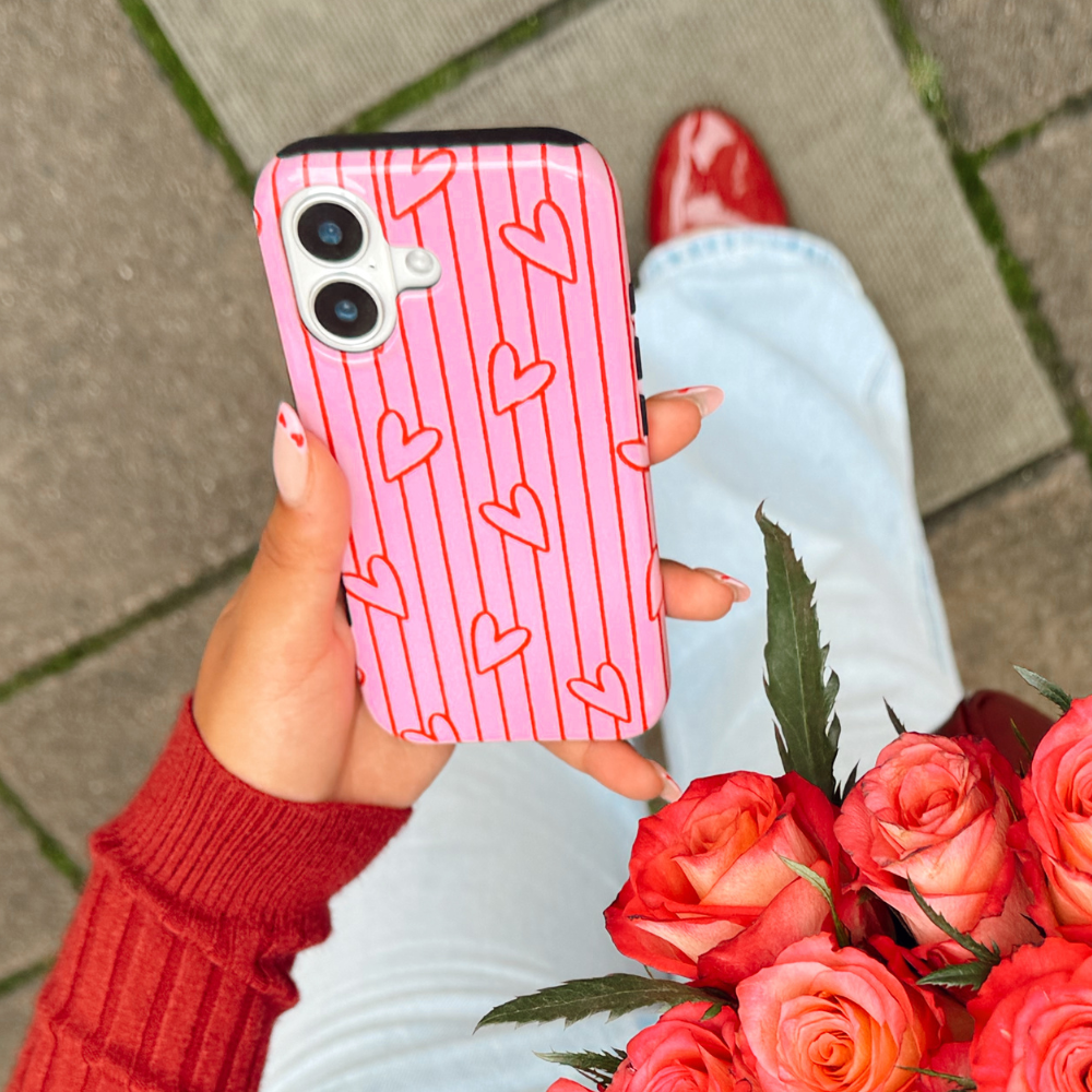 Person holding a phone with a pink heart pattern case, and roses, with red shoes and light blue jeans.