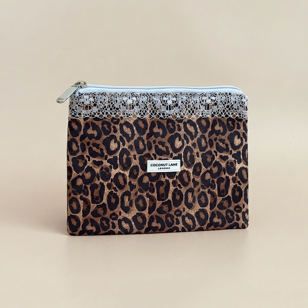 Leopard print zip pouch with a pale blue lace trim along the top, a pale blue zip with a silver pull, and a white Coconut Lane London logo badge on the front, shown on a beige background.