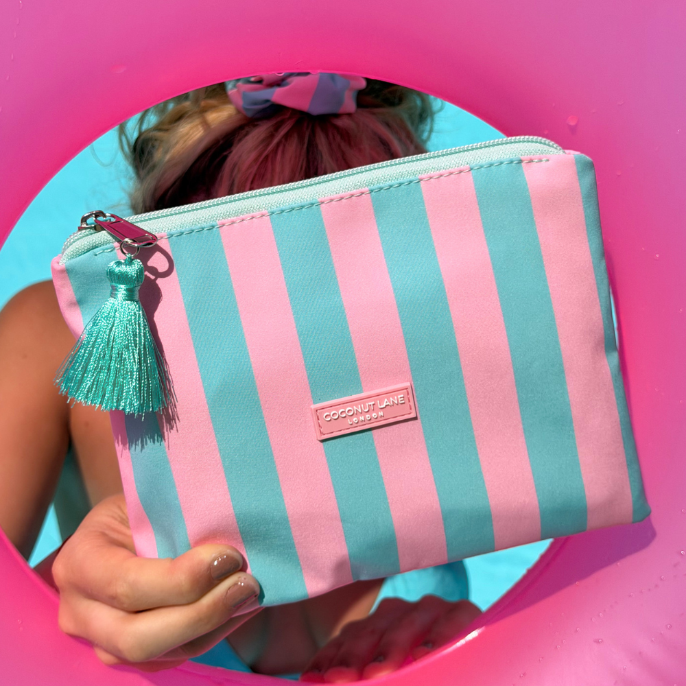 Pink and blue striped Mini Pouch with a tassel held by a person against a pink background