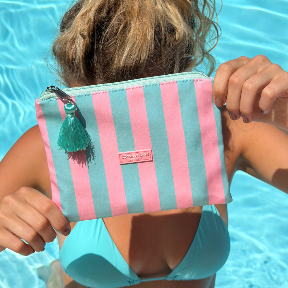 Girl holding a striped palm springs mini pouch with a tassel in front of a pool.