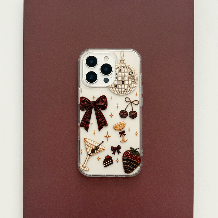 A clear phone case decorated with party-themed graphics including a large burgundy bow, a martini glass, cherries, a strawberry, a disco ball, and small gold stars.