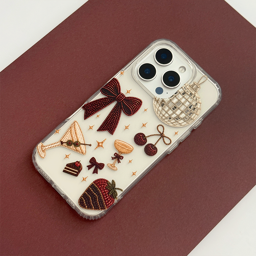 A clear phone case decorated with party-themed graphics including a large burgundy bow, a martini glass, cherries, a strawberry, a disco ball, and small gold stars.