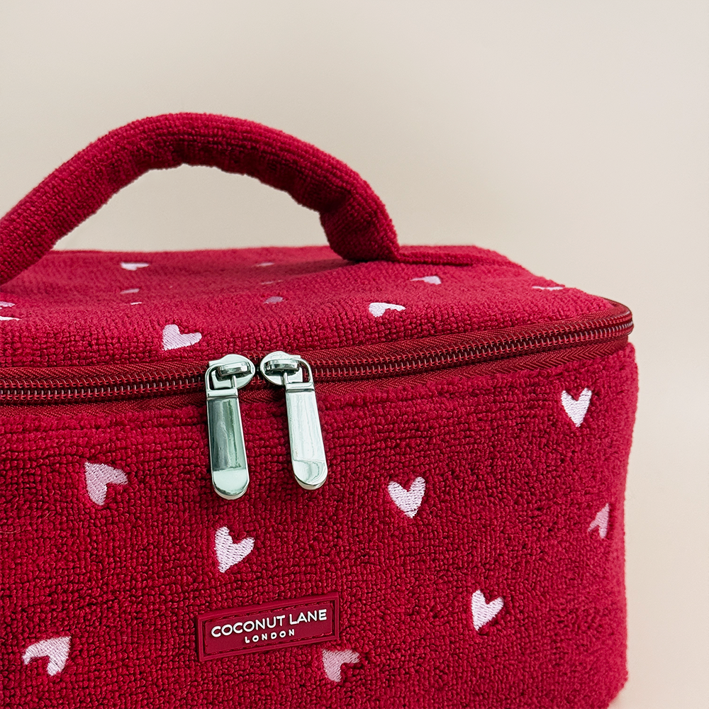 Red cosmetic bag with heart patterns and 'Coconut Lane' branding on a beige background