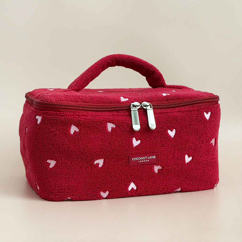 Red cosmetic bag with white heart patterns on a beige background