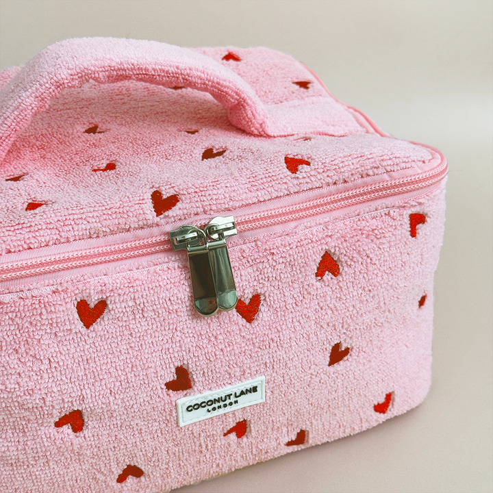 Pink textured travel case with red heart patterns and a visible brand label on a light background