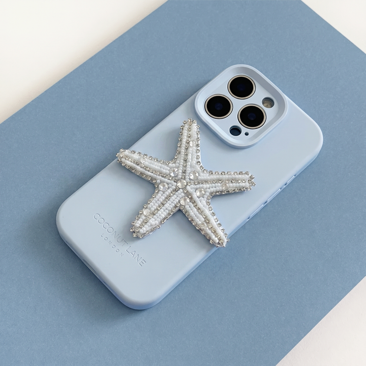 White and silver 3D starfish made from beads and sequins, on top of a blue Coconut Lane Phone Case. 