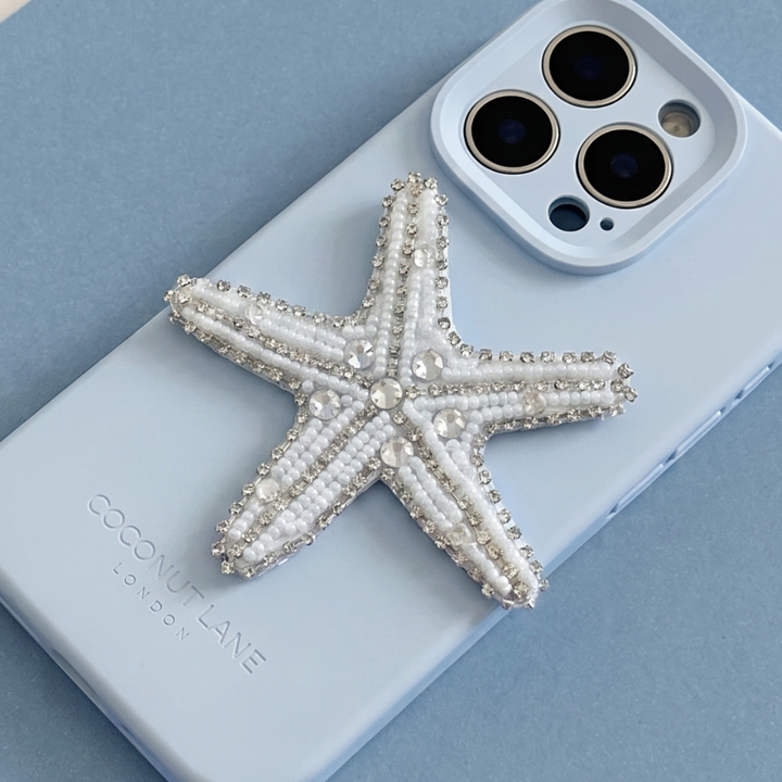 White and silver 3D starfish made from beads and sequins, on top of a blue Coconut Lane Phone Case. 
