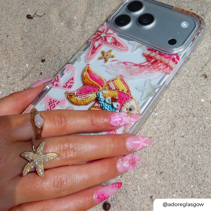 Pink Paradise Phone case with colorful designs held by a hand on sandy ground