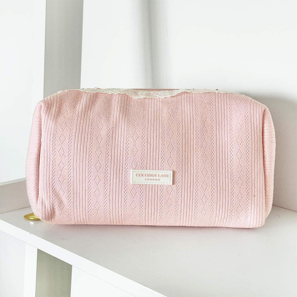 Pink pointelle fabric makeup bag with Coconut Lane logo badge. White lace trim detailing.