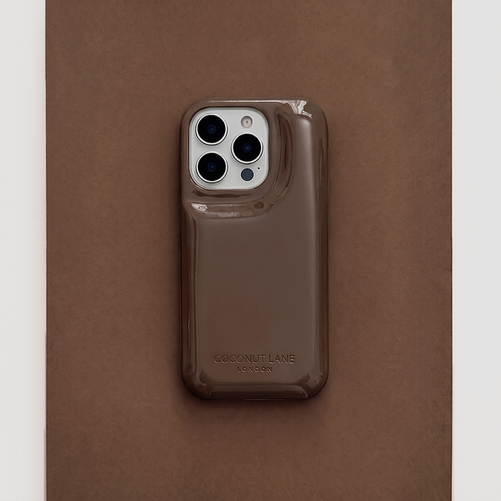 Glossy chocolate brown Coconut Lane puffer phone case with embossed logo, displayed diagonally on a matching brown background.