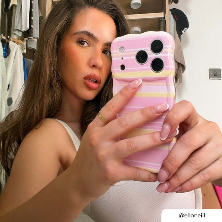 Woman taking a mirror selfie, holding an iphone in a pink, white and yellow horizontal striped wavy phone case.