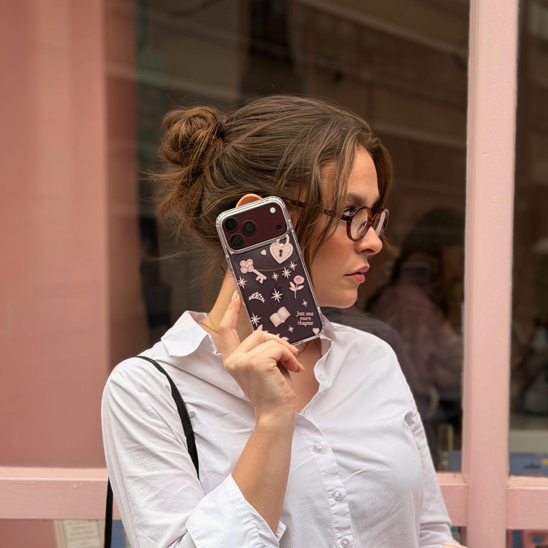 Woman holding a burgundy iphone. The iphone is in a Romance Girly Clear Phone Case showing intricate pink key, heart padlock, floral and star details with clear edges.