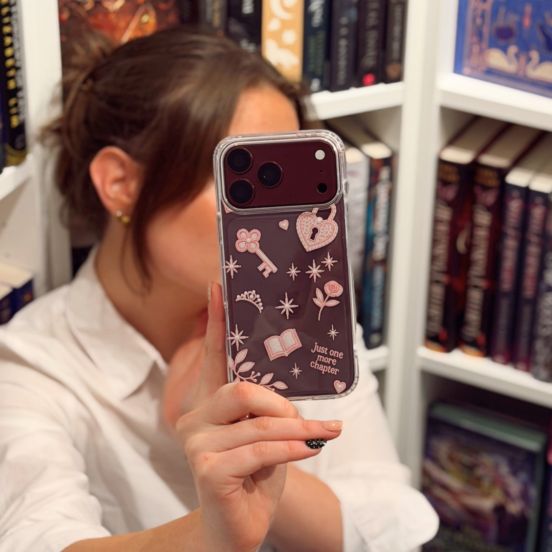 Woman in bookstore taking a selfie with a burgundy iphone. The iphone is in a Romance Girly Clear Phone Case showing intricate pink key, heart padlock, floral and star details with clear edges.