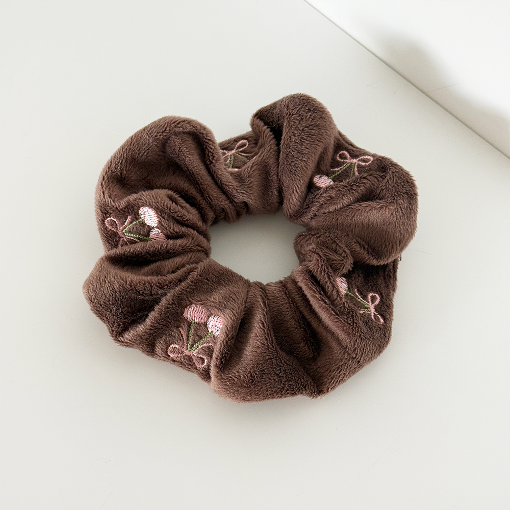 Scrunchie made from soft, fluffy chocolate brown fabric with delicate pink cherry embroidery and green stems, photographed on a white background.