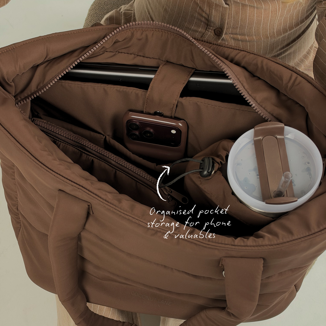 Close-up image of the inside of the Main Carry Choc Brown Puffer Bag showing the compartments and storage for iphone and valuables. Inside the bag is a Coconut Lane Chocolate Brown tumbler and the Chocolate Brown Puffer PC.