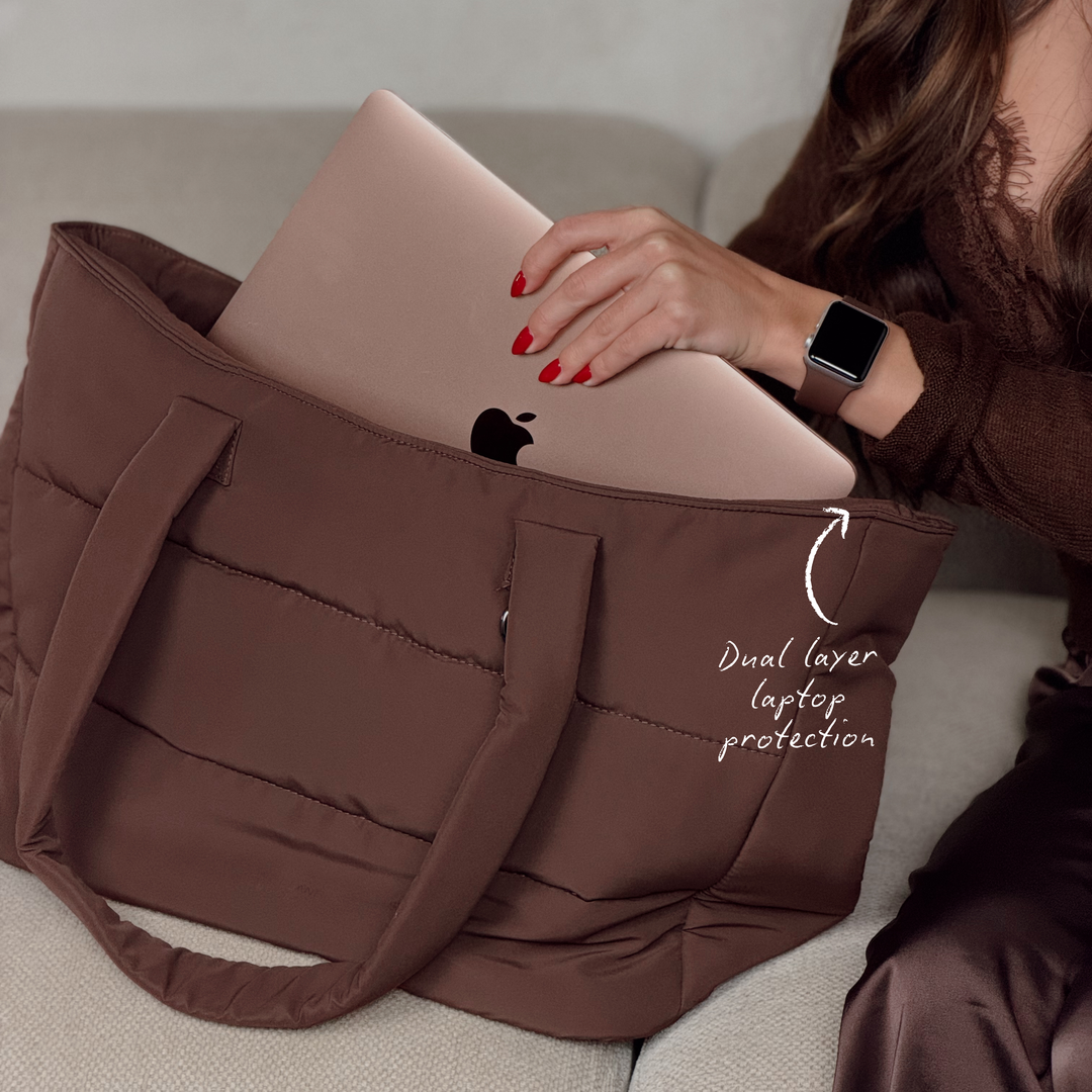 Close-up image of the Main Carry Choc Brown Puffer Bag showing the dual layer laptop protection compartment. On the woman's wrist is a Coconut Lane NAKD apple watch strap in chocolate brown. 