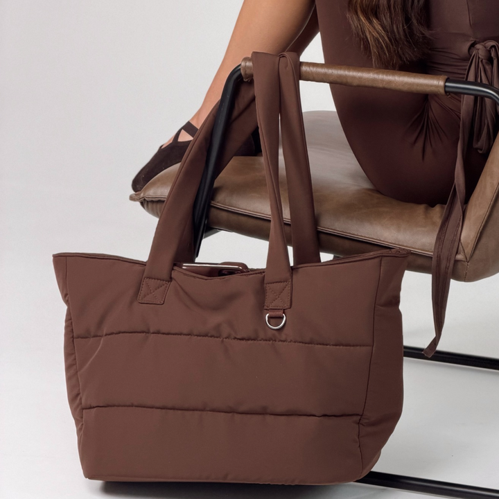 Close-up studio shot of the chocolate brown padded tote bag with quilted panels, long shoulder straps and metal d-ring detail.