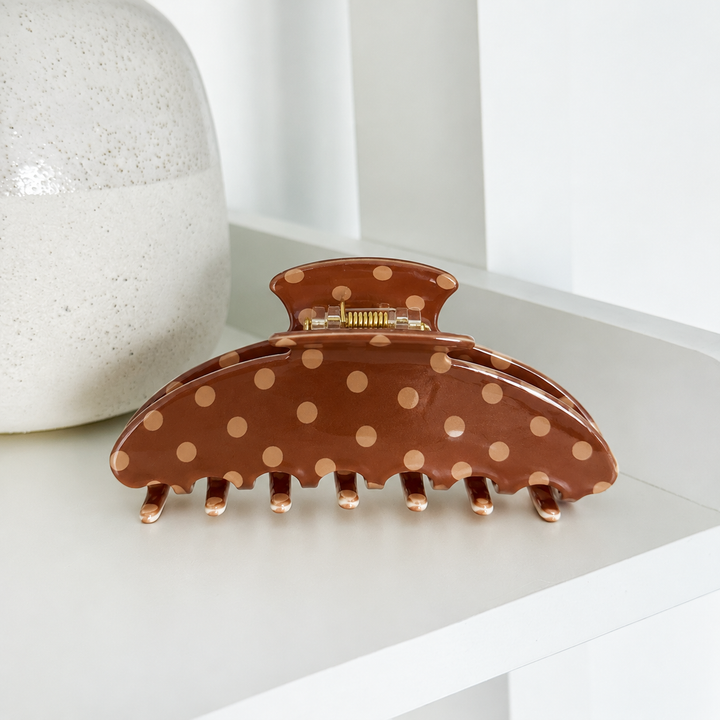 Claw Clip featuring a glossy chocolate brown finish with beige polka dots, curved teeth and a gold-toned spring hinge, photographed on a white shelf.