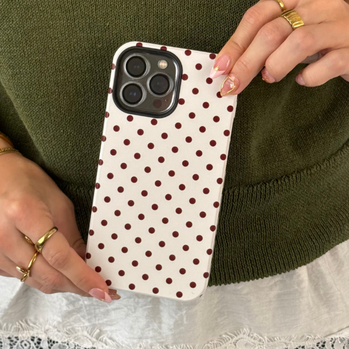 Woman in a dark green jumper, with white lace shirt underneath, holding an iphone in a cream and brown polka dot case. 