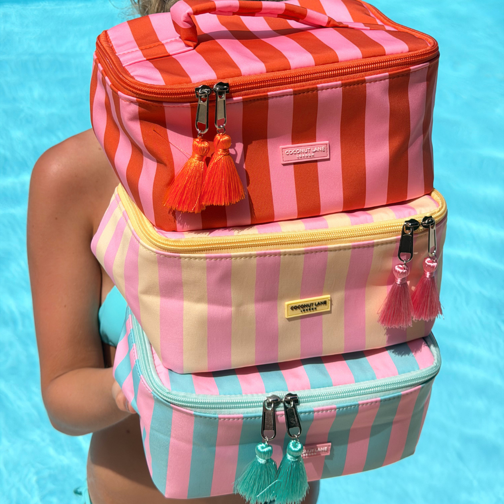 Stack of three striped vanity cases with tassels against a blue water background